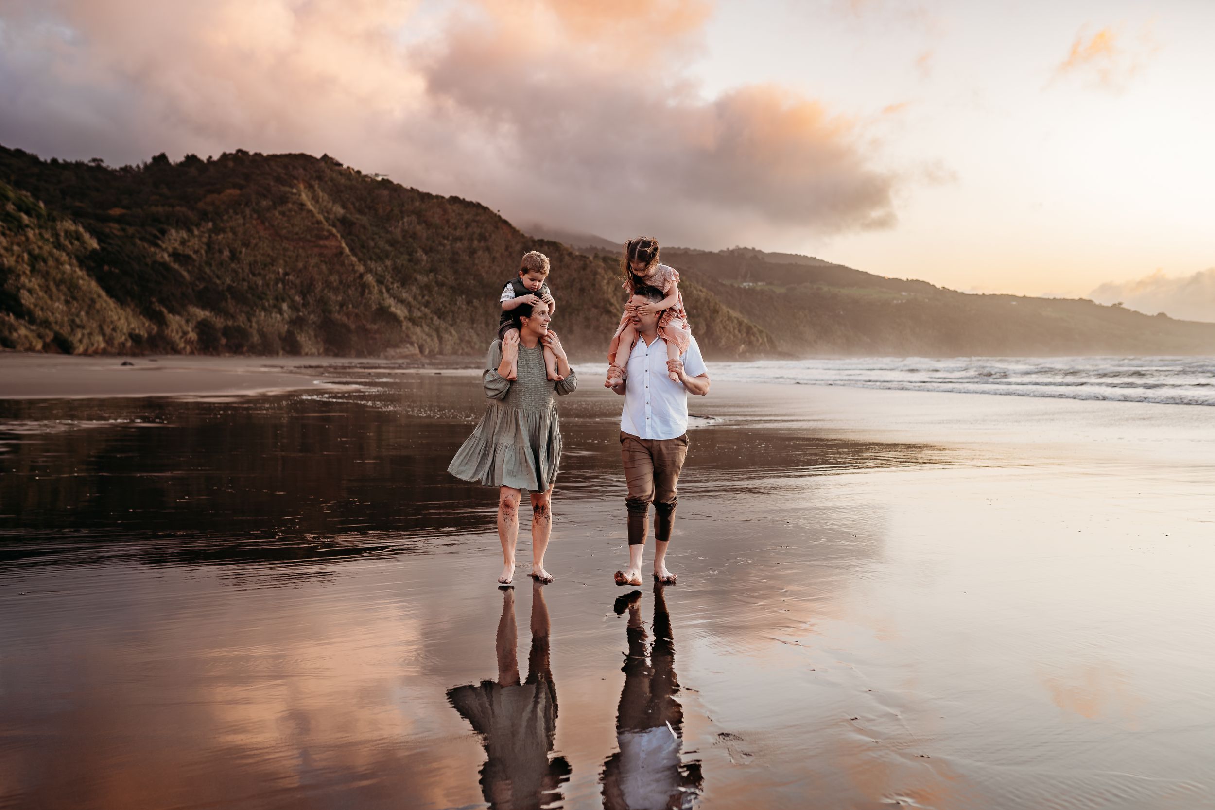 Two figures walking together on a scenic beach at sunset with mountains in the background.