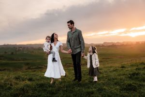 Family standing together in field during golden sunset.