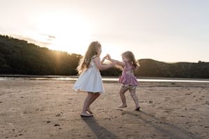Two children dancing together on beach at sunset.
