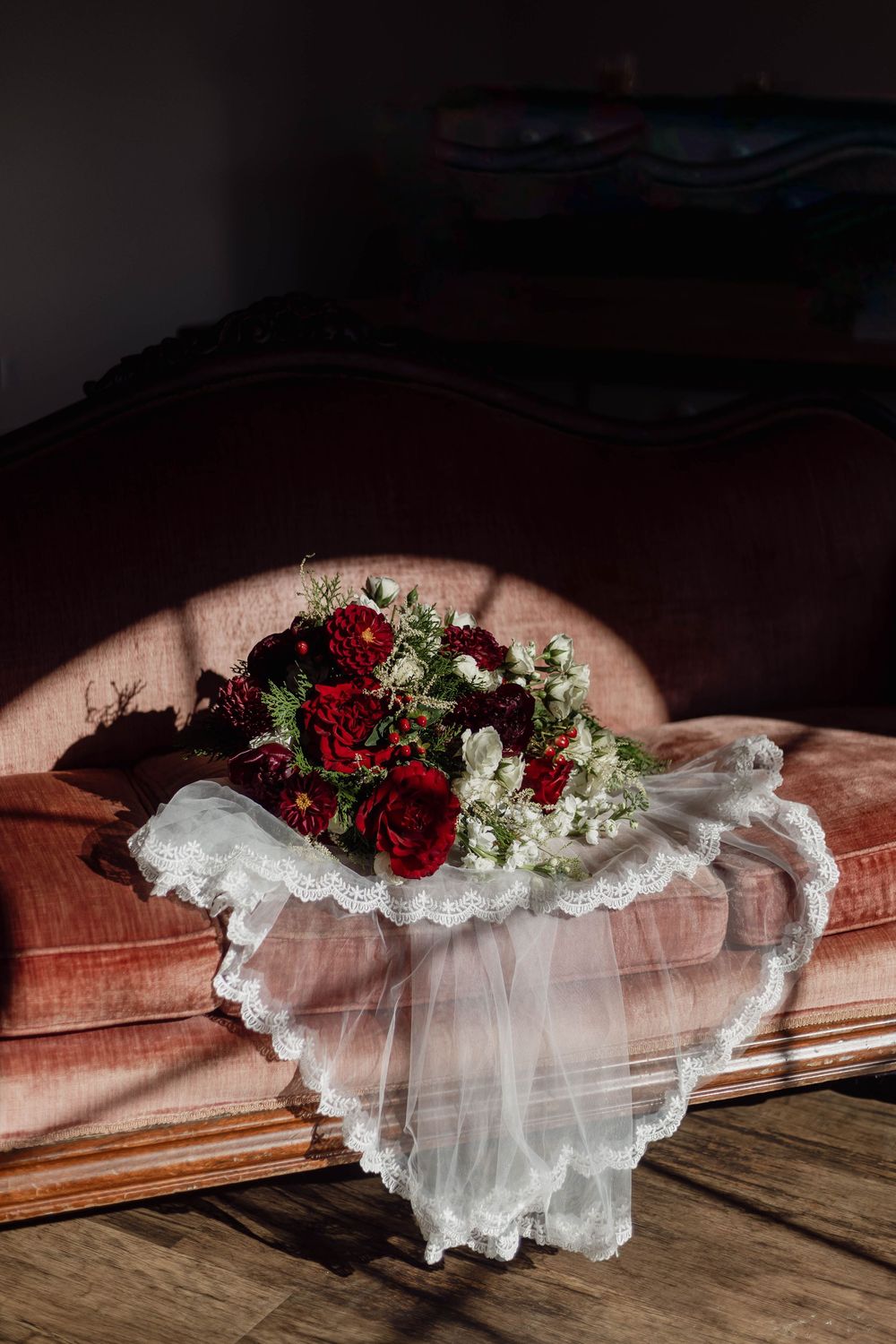 A white lace garter adorned with red roses and greenery lies on a wooden surface in dramatic lighting.