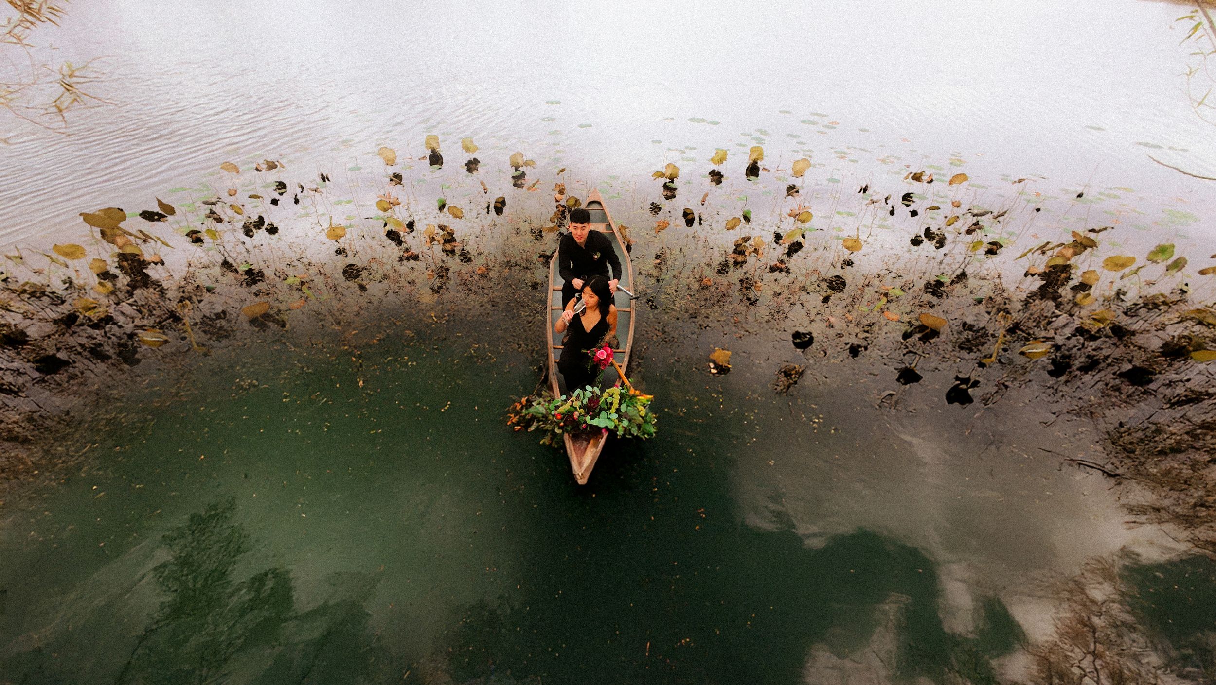 Aerial view of a kayaker paddling through green waters surrounded by autumn leaves floating on the surface.