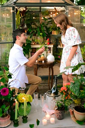 Proposal scene in a decorated greenhouse with candles, flowers and champagne.