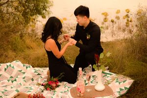 Couple enjoying a romantic outdoor picnic with tea and treats on a pink tablecloth at sunset.