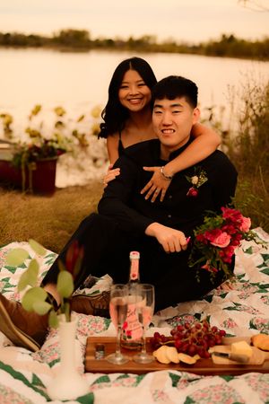 A romantic sunset picnic setup with wine glasses, flowers and a cozy blanket by the water.