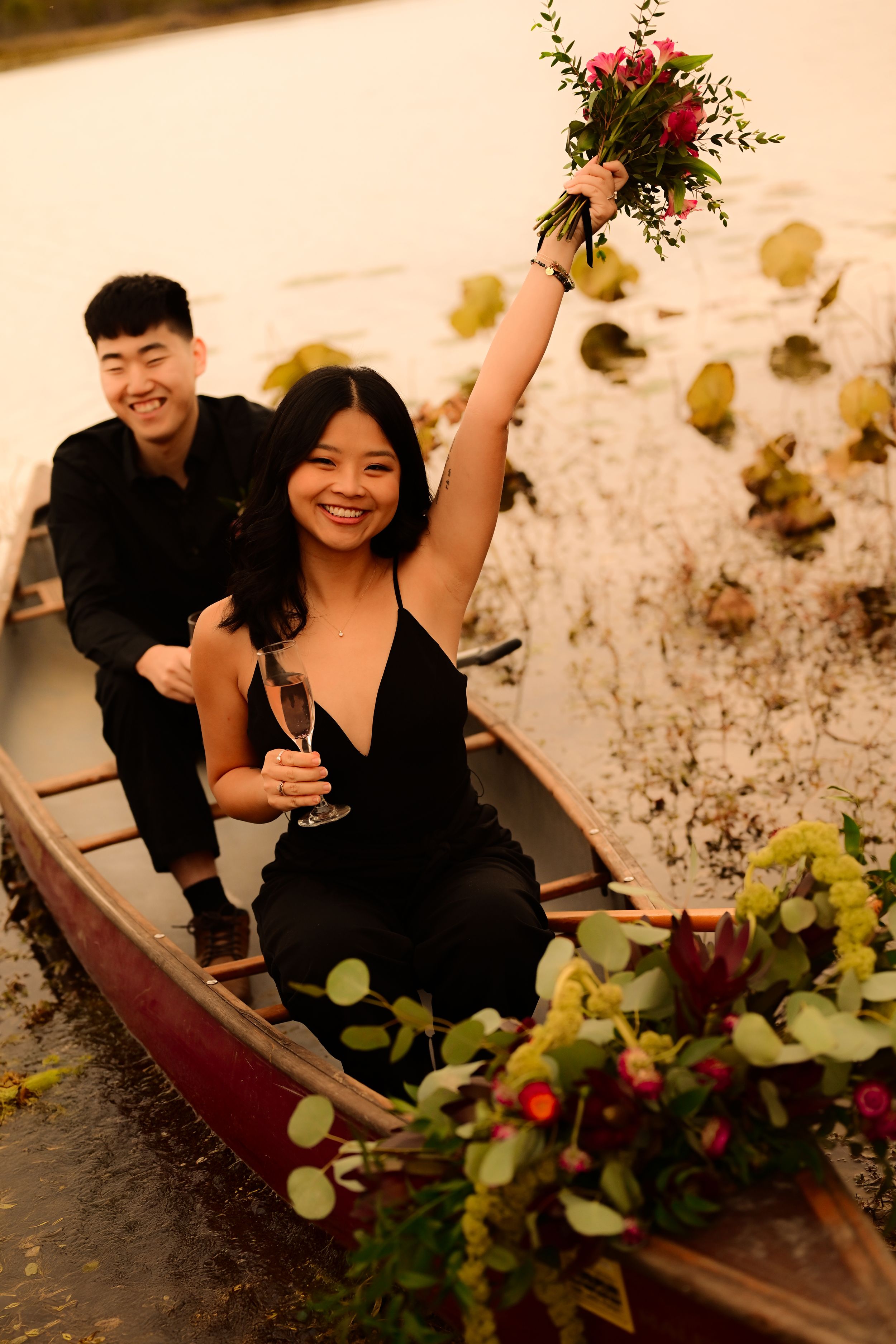 Romantic couple sitting in wooden canoe decorated with greenery and flowers during sunset photo session.