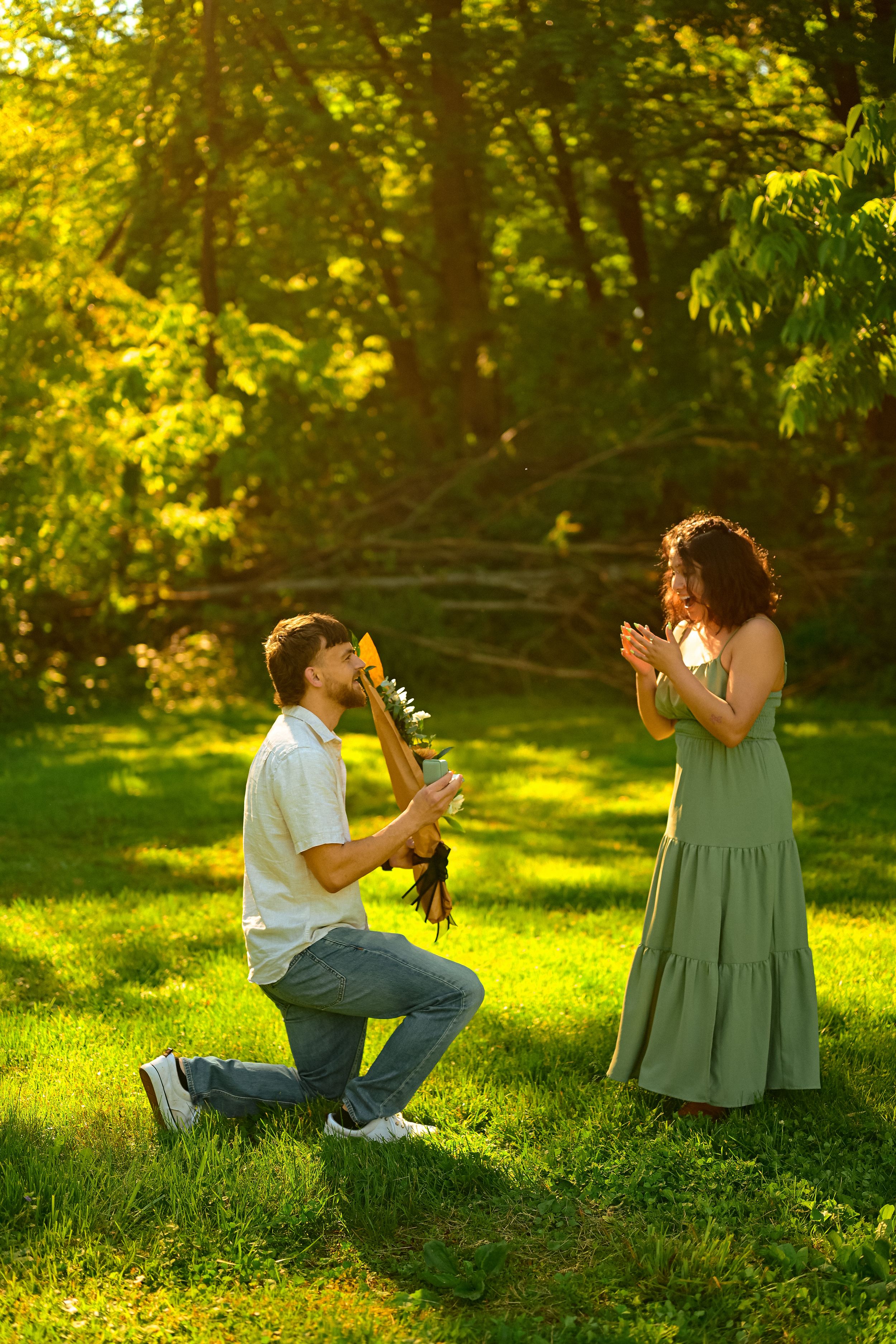 A romantic outdoor proposal scene with someone kneeling and presenting flowers in a sunlit garden setting.