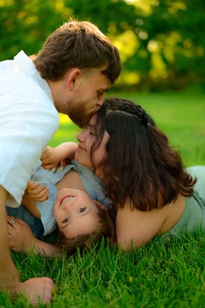 A family shares a tender moment while laying in green grass on a sunny summer day.