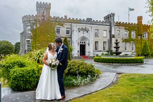 A wedding celebration takes place at a majestic stone castle with grey walls and turrets on a cloudy day.  Castle Bellingham County Louth