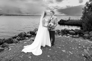 A couple in wedding attire poses together on a rocky beach shoreline with ocean waves in the background.  Crover House Hotel Cavan.