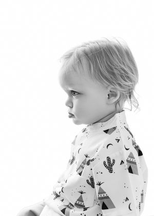 Black and white portrait of a toddler in a patterned onesie with cacti and teepees, looking sideways.