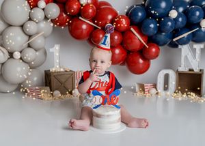Red white and blue balloon arch decorates a first birthday celebration setup with wooden crates and festive party decor.