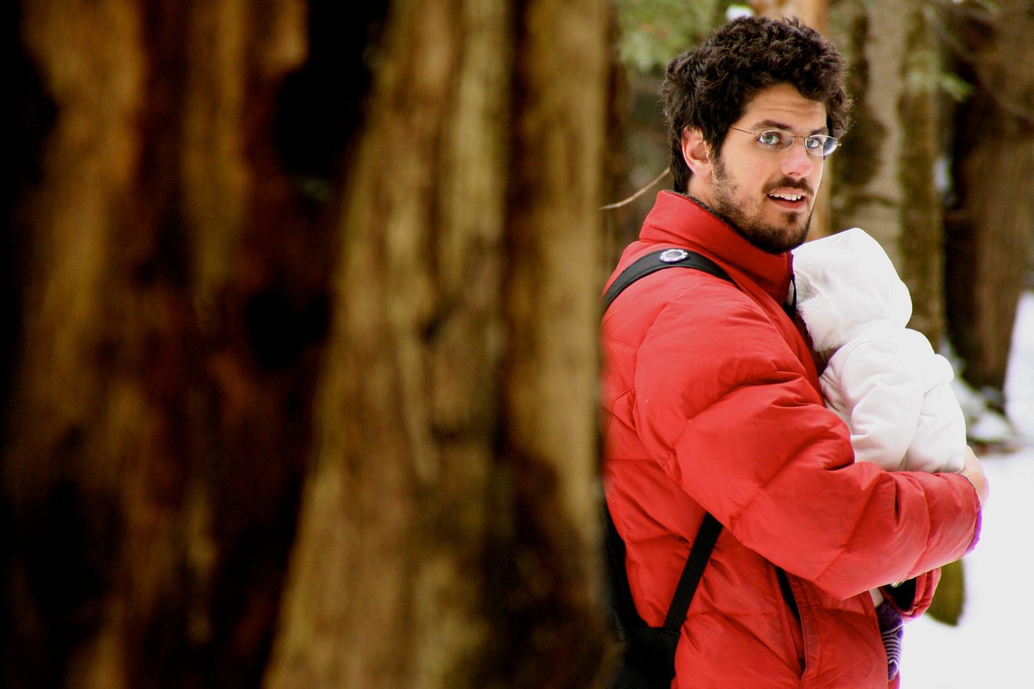 A person in a red jacket walking through a forest of tall trees.