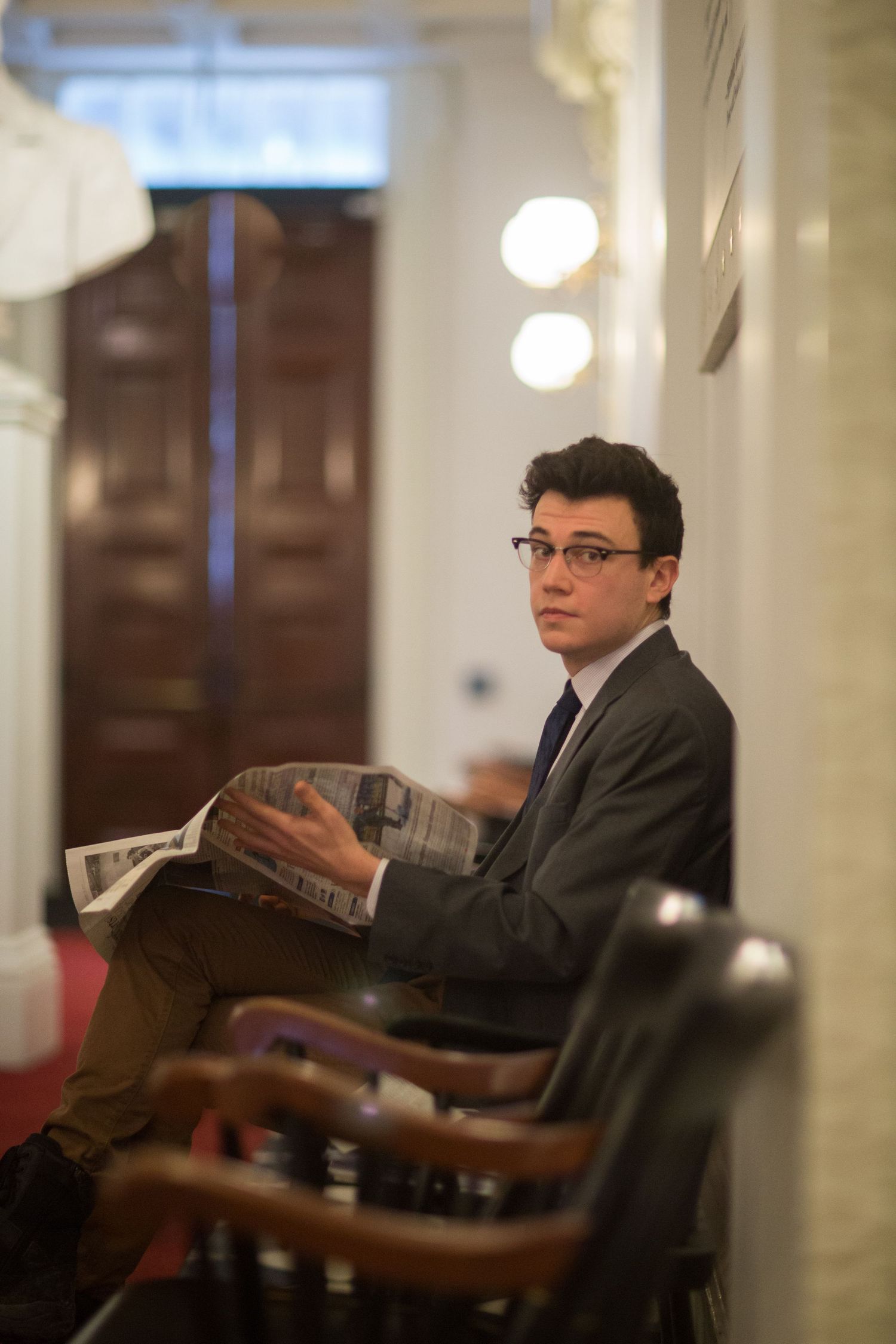 A person in a suit sitting in a formal setting while reading documents.