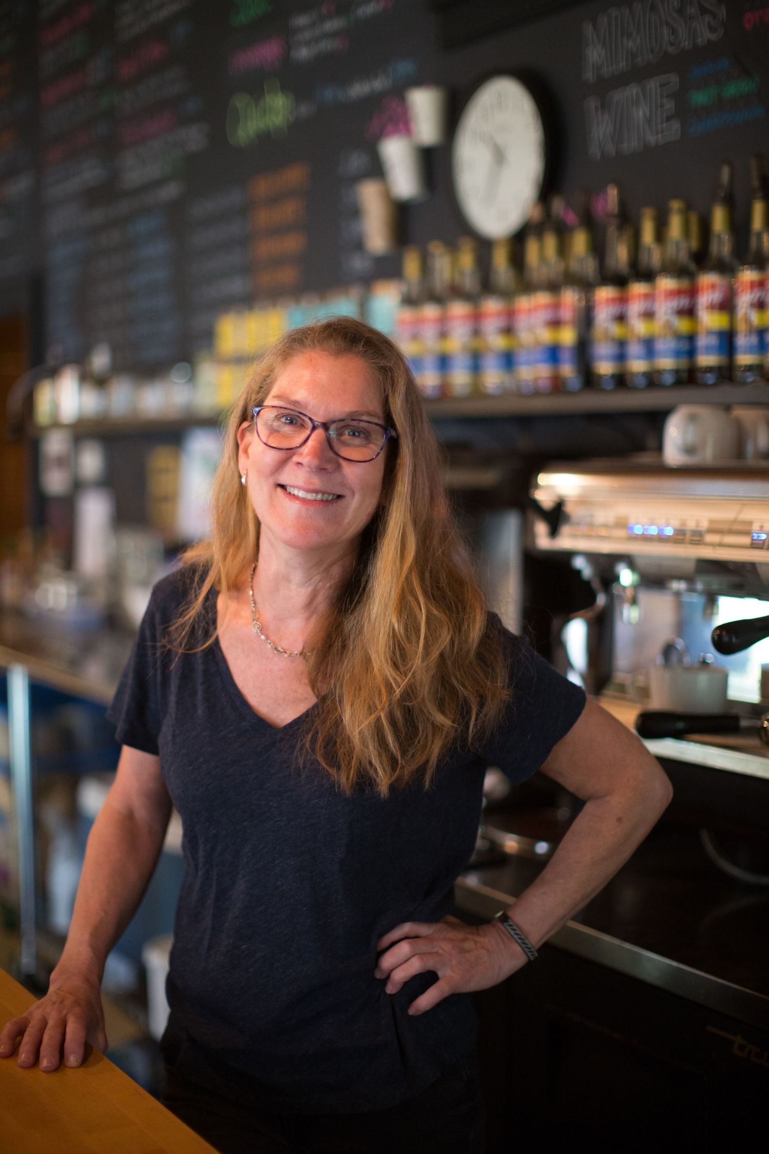 A person posing at a bar with bottles and taps in the background.