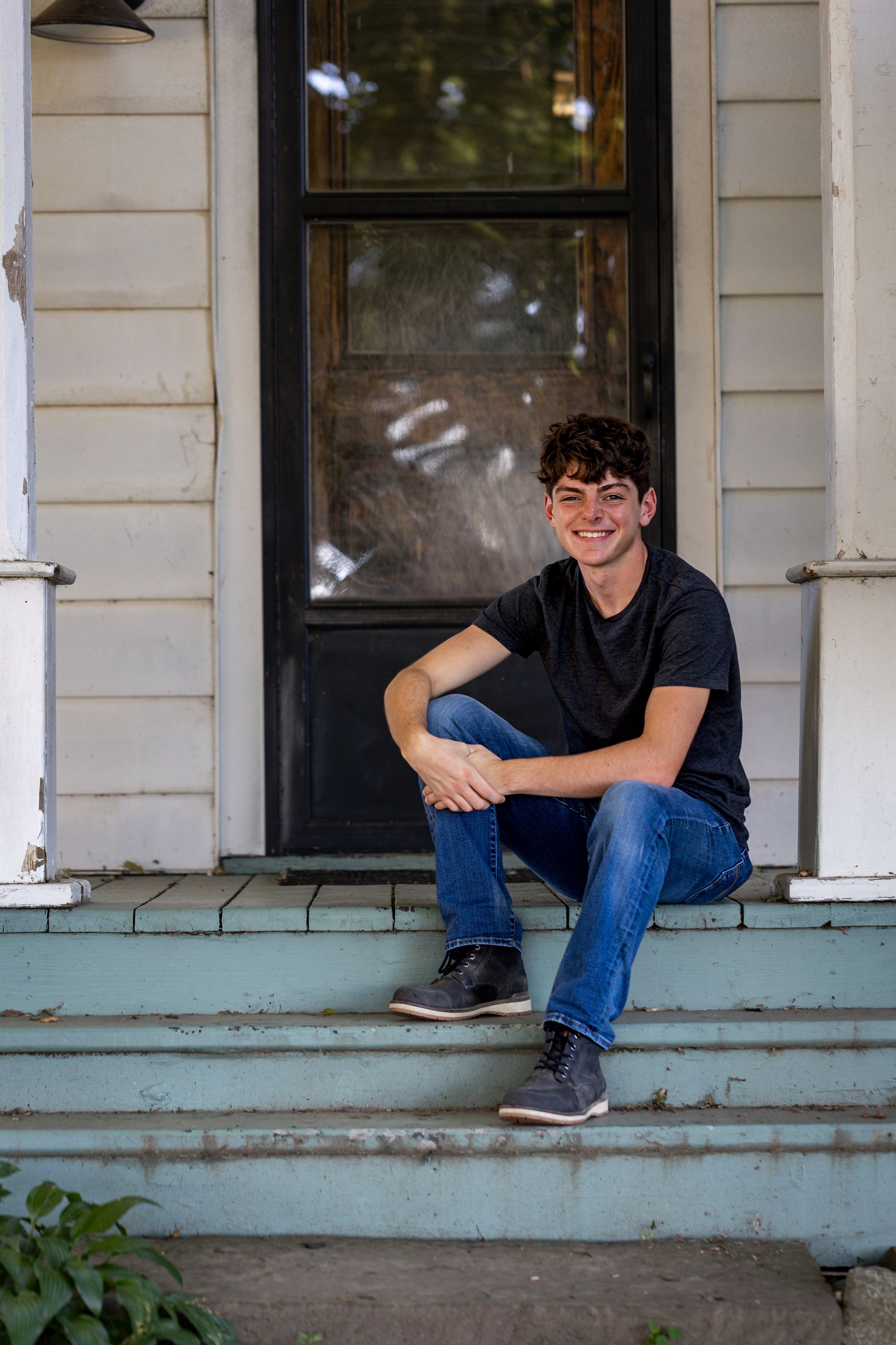 Smiling teen boy in black t-shirt sitting on house porch steps.
