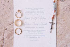 Wedding invitation with three gold rings and a delicate beaded bracelet arranged on textured paper.