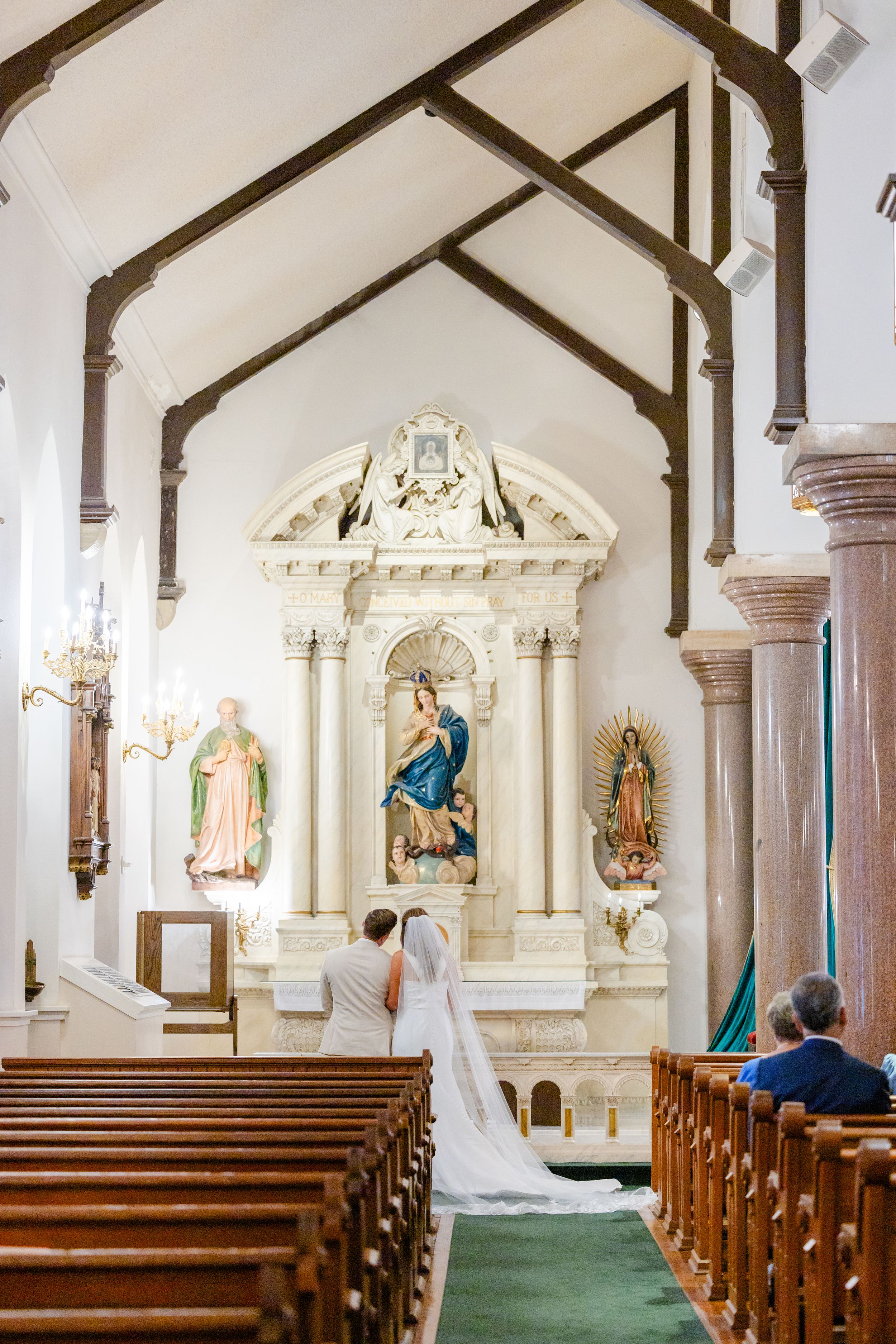 Interior of Catholic church with ornate altar and religious statues during wedding ceremony.