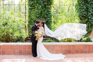 A flowing white veil catches the breeze in a lush garden setting with ivy-covered walls.