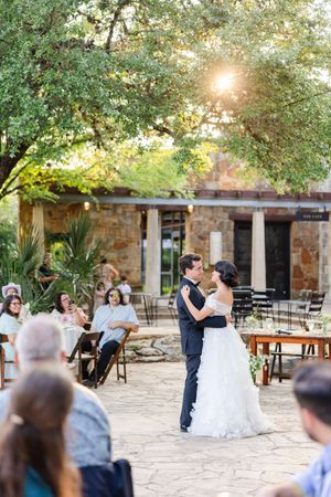 A couple shares a romantic dance outdoors at a rustic stone venue during a sunset wedding celebration.
