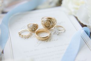 Golden wedding rings displayed among cream colored petals and decor elements with soft blue accents.