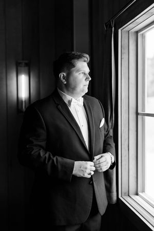 A person in a black suit gazes thoughtfully through a window in this dramatic black and white composition.