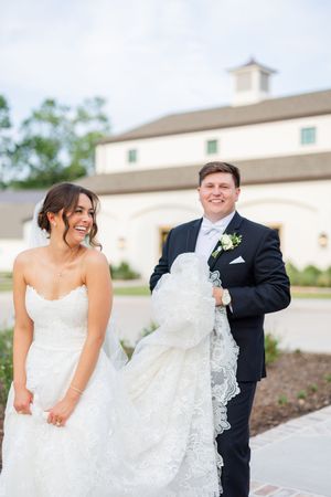 A joyful wedding couple shares a candid moment outdoors in front of a white barn on their special day.