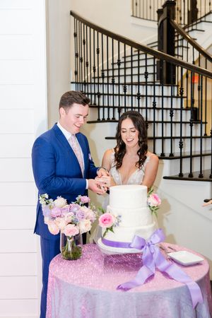 Wedding couple cuts into their elegant purple and white tiered cake at their reception celebration.