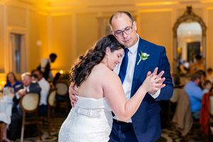 A couple dancing together at an elegant ballroom wedding reception with warm amber lighting.
