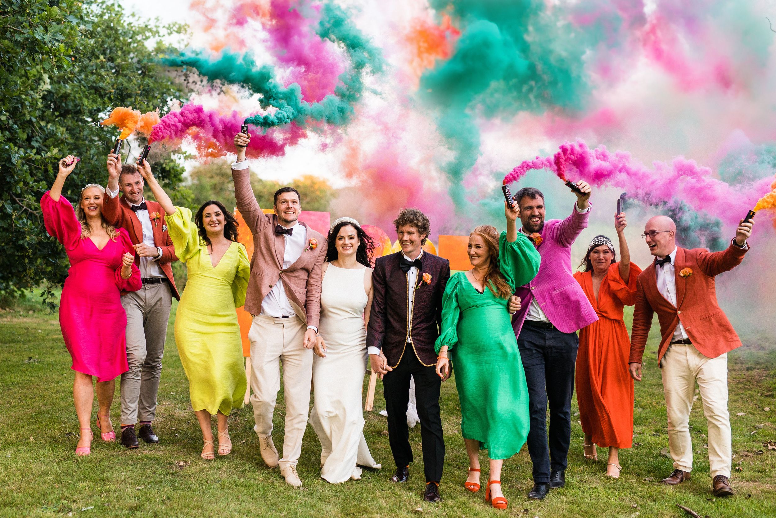 Wedding couple celebrating with friends beneath clouds of colourful smoke at a festival-style wedding