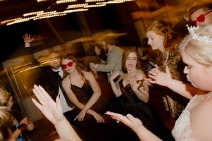 Wedding guests wearing fun red heart sunglasses celebrate and clap at a lively reception dance party.