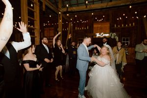 Bride and groom dance joyfully surrounded by cheering guests at a rustic barn wedding reception.