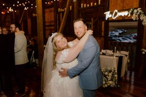Bride in white lace gown and groom in light blue suit share a warm embrace during wedding reception.