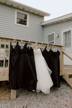 White wedding dress and black bridesmaid dresses hanging on hangers outside building.
