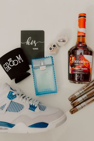 Groom wedding flat lay with Jordan sneakers, Hennessy, cologne, vow book, and rings.