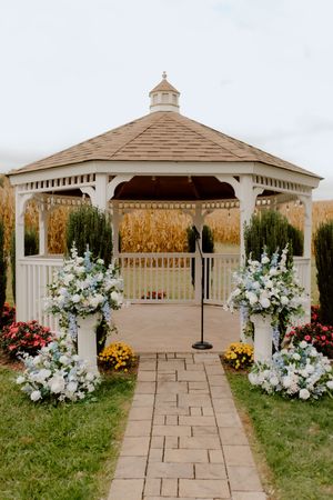 White gazebo wedding ceremony entrance with blue and white floral arrangements on pillars.