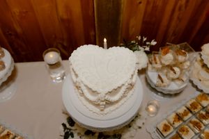 Heart-shaped white wedding cake with candle on dessert table with treats.
