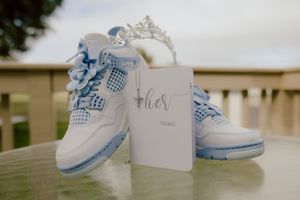 Blue and white Jordan 4 sneakers with tiara and wedding vow card on table.