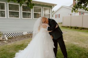 Groom in black suit shares tender embrace and kiss with bride in white lace gown during first look.