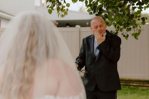 Groom wipes away tears of joy while seeing bride in white wedding gown during emotional first look moment.