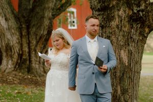 Bride and groom read heartfelt vow letters to each other beside a large tree before their ceremony.