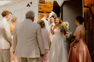 Bride and groom greeted by wedding guests at barn venue entrance.