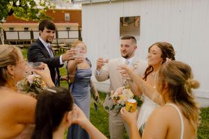 Bride and groom toasting with wedding party outdoors, bridesmaids in blue and white dresses holding champagne glasses.