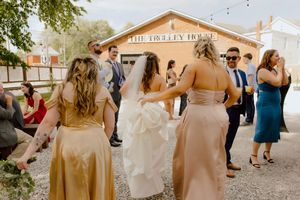 Bride in white gown with bridesmaids in gold dresses walking toward The Trolley House wedding venue.