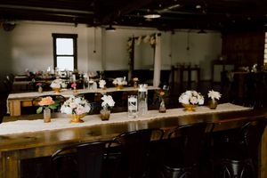 Elegant wedding reception table decorated with white floral centerpieces, candles, and burlap runner in rustic venue.