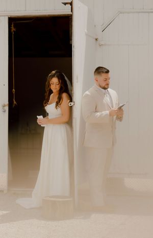 Bride and groom reading private vows separately on opposite sides of a white barn door before their ceremony.