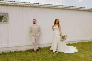Bride and groom pose separately against white barn wall on wedding day.