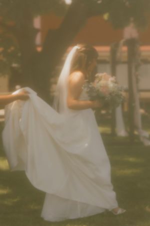 Dreamy soft-focus bride twirling white gown while holding bouquet outdoors.