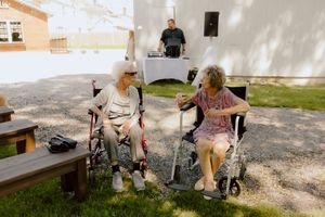 Two elderly women in wheelchairs chat together at outdoor wedding reception.