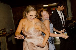 Bridesmaids in champagne satin dresses dance and laugh together at a lively wedding reception party.