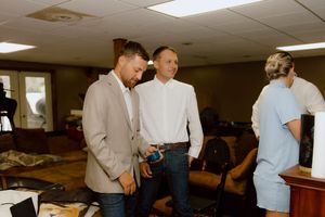 Two groomsmen in tan blazers chatting casually indoors while getting ready before the wedding ceremony.
